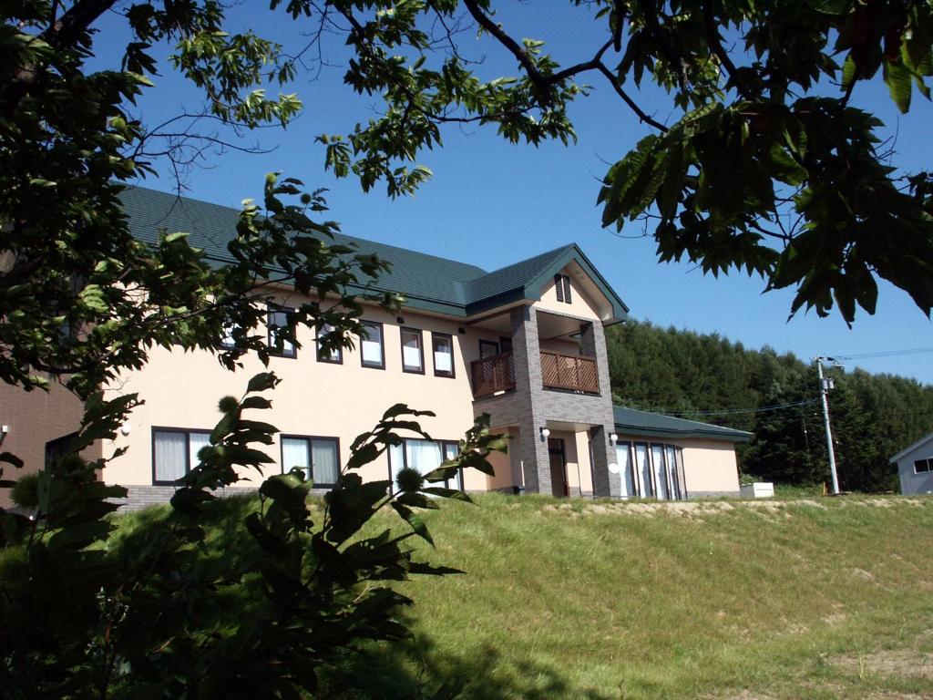 duży biały dom na wzgórzu z drzewami w obiekcie Pension and Restaurant La Collina w mieście Nakafurano