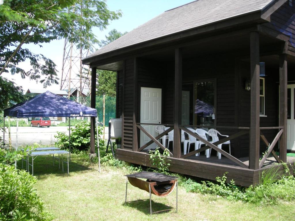 une maison avec une terrasse couverte dotée de chaises et d'un parasol dans l'établissement Villa Komakusa, à Hakuba