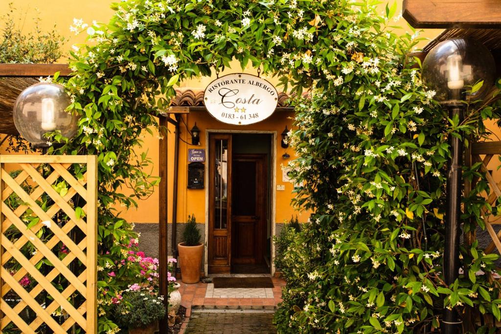 une entrée à un bâtiment jaune avec une arche de fleurs dans l'établissement Albergo Costa, à Imperia