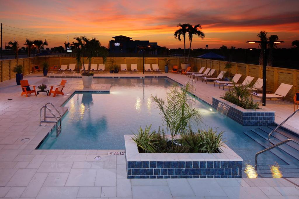 a swimming pool with chairs and a sunset in the background at Hotel Indigo Orange Beach - Gulf Shores by IHG in Gulf Shores