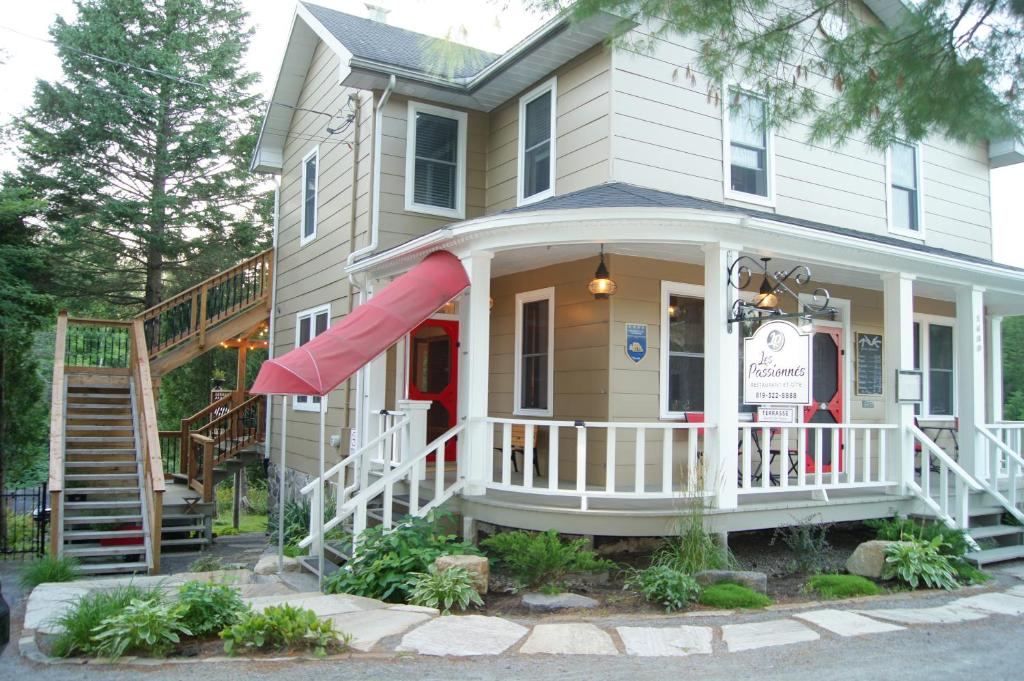 une maison blanche avec une terrasse couverte dotée d'un auvent rouge dans l'établissement Restaurant et Gite Les Passionnés, à Val-David