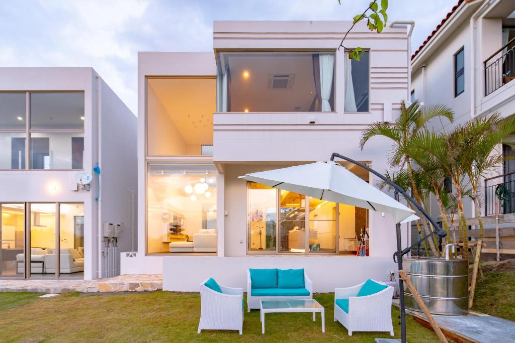 a white house with blue chairs and an umbrella at Ocean Villa Fuchaku Okinawa in Fuzuchi