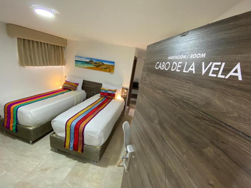 2 camas en una habitación de hotel con un cartel en la pared en San Bernardo Hotel en Riohacha