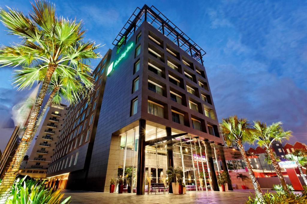 Holiday Inn Santo Domingo, an IHG Hotel في سانتو دومينغو: فندق فيه نخل امام مبنى