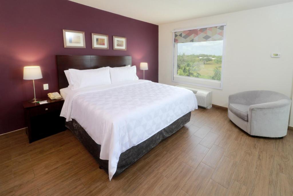レイノサにあるHoliday Inn Reynosa Industrial Poniente by IHGのベッドと椅子と窓のある寝室
