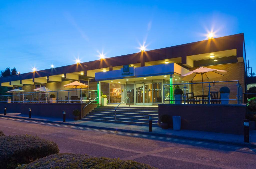 un bâtiment avec des tables et des parasols devant lui dans l'établissement Holiday Inn Rugby-Northampton M1 Jct18, an IHG Hotel, à Crick