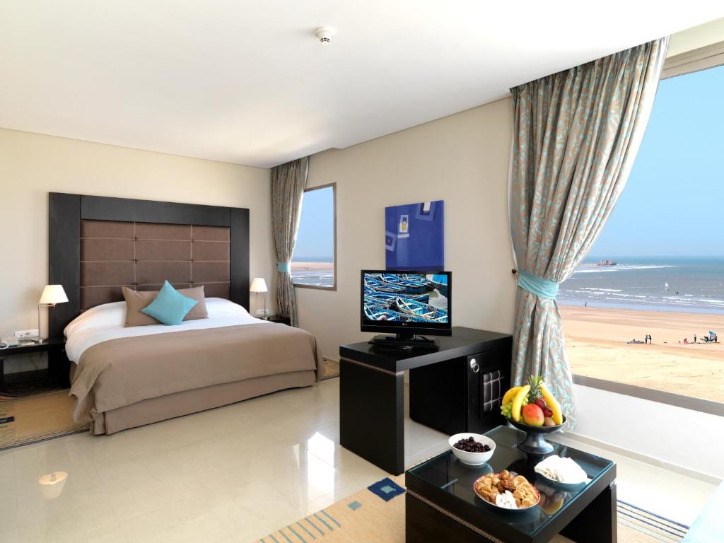 una camera con letto e televisore e una spiaggia di Atlas Essaouira Riad Resort a Essaouira