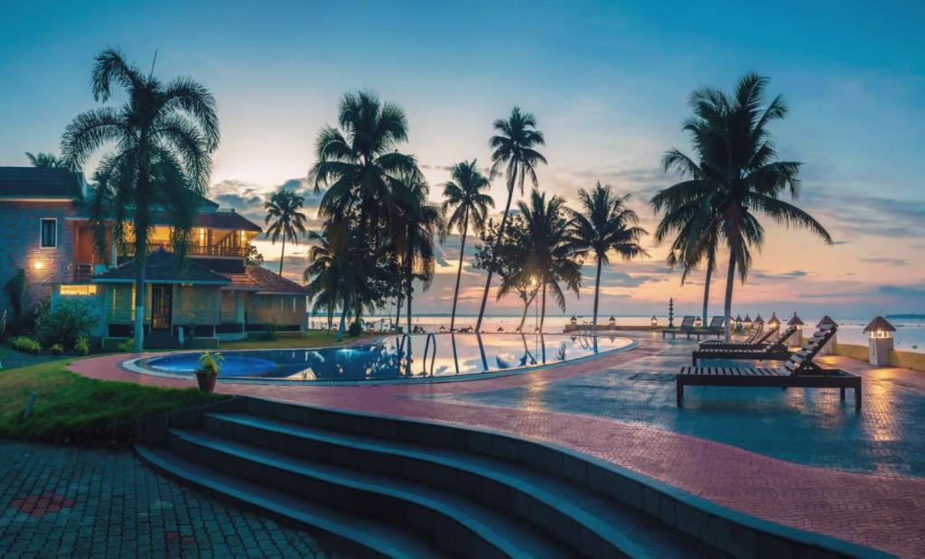 ein Resort mit einem Pool und Palmen bei Sonnenuntergang in der Unterkunft The World Backwaters, Alleppey in Kumarakom