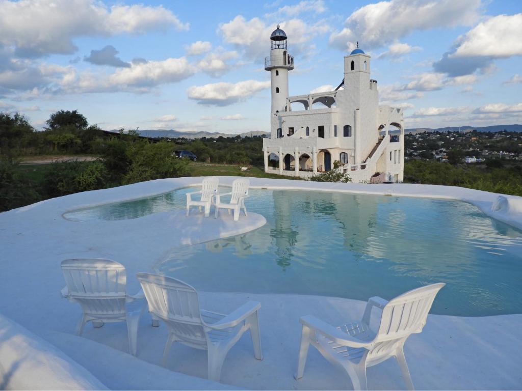 a pool with chairs and a lighthouse in the background at El Faro de Carpier - ApartHotel & Restaurante Bar Cafetería in Tanti