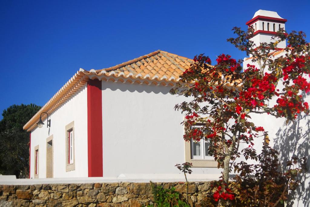 een wit huis met een rood dak en een boom met rode bloemen bij Casas da Tia Alice in Mafra