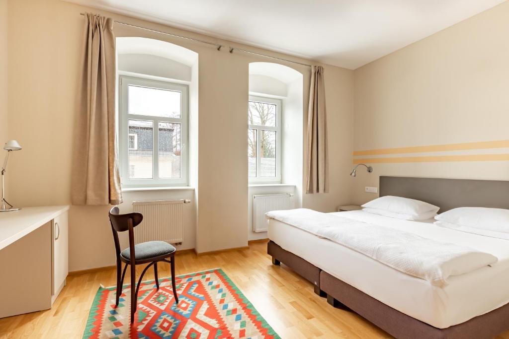 a bedroom with a bed and a chair and two windows at Boutique Hotel SwissHouse in Mariánské Lázně