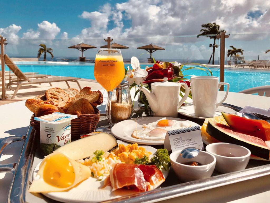a tray of breakfast food on a table next to a pool at Hôtel Exsel Créolia in Saint-Denis