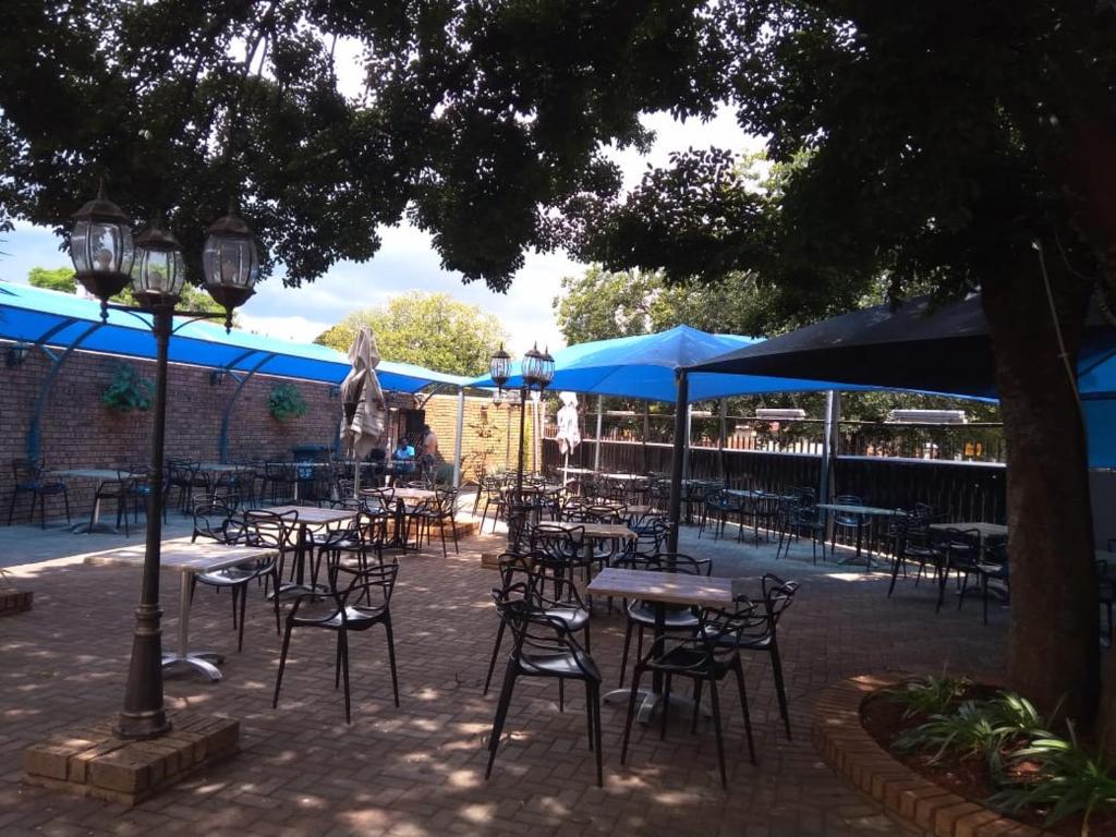een groep tafels en stoelen met blauwe parasols bij Suits Guest house & bar in Carletonville