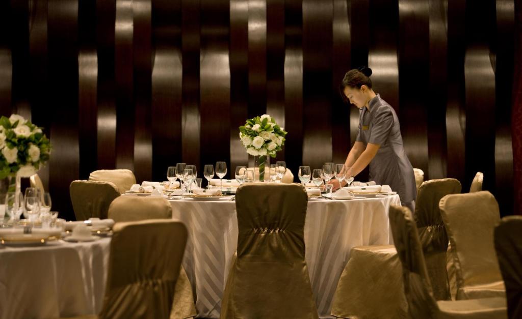 uma mulher em pé em frente a uma mesa com mesas brancas em Crowne Plaza Tianjin Binhai, an IHG Hotel em Tianjin