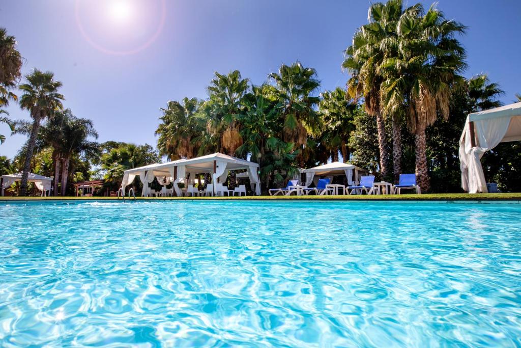 uma piscina num resort com palmeiras e guarda-sóis em Hotel Tancat de Codorniu em Les Cases d'Alcanar
