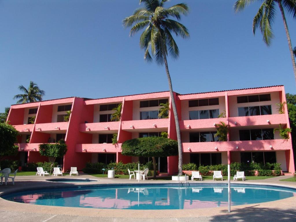 a pink building with a swimming pool and palm trees at Coral Ixtapa in Ixtapa
