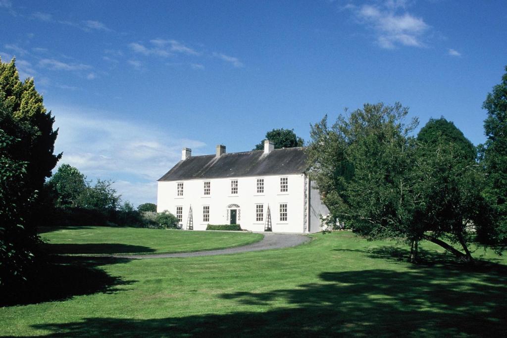 a white house on a green field with trees at Ballymote Country House in Downpatrick