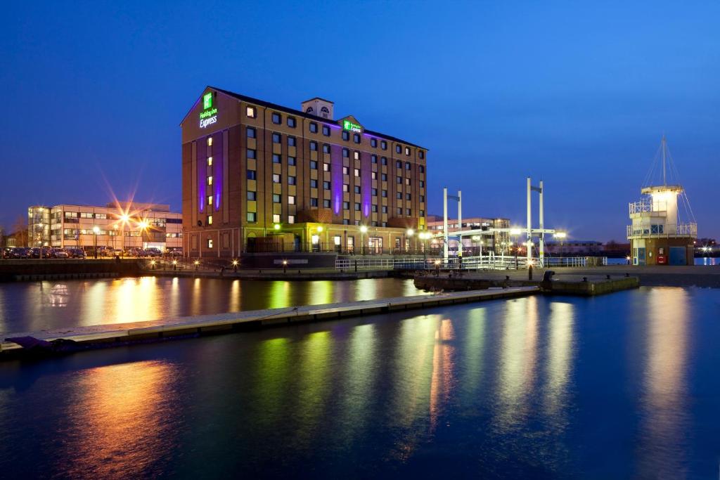a building is lit up at night on a river at Holiday Inn Express Manchester - Salford Quays, an IHG Hotel in Manchester