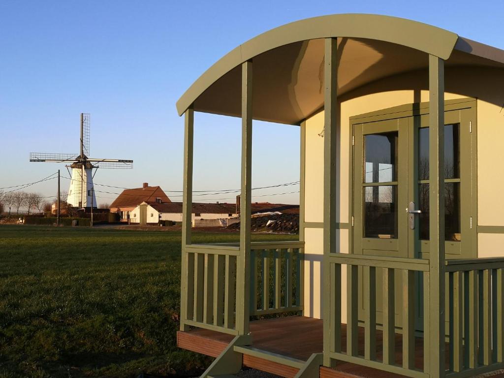 a small gazebo in a field with a windmill at Roulotte Hartemeers in Tielt