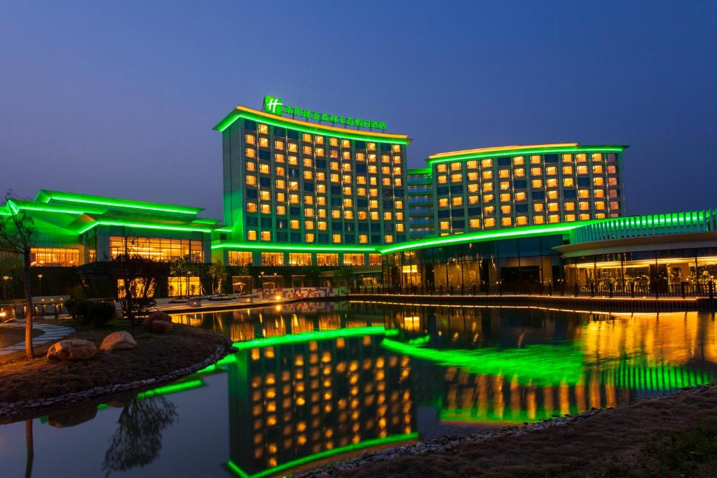 a building with green lights in front of a body of water at Holiday Inn Nanyang by IHG in Nanyang