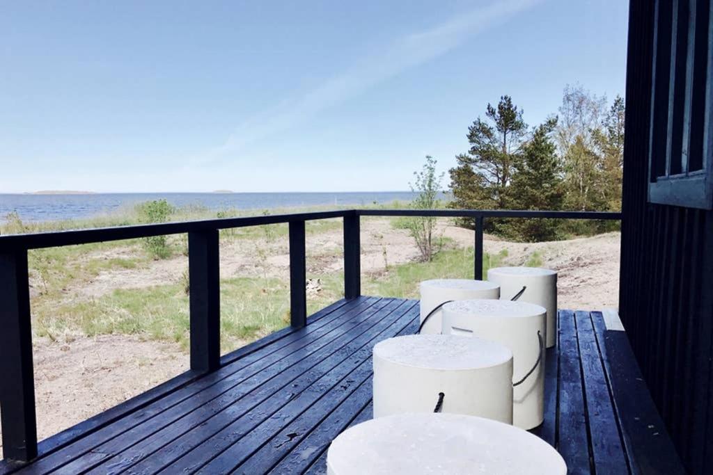 a balcony with four white stools and a view of the beach at H A R R B Å D A - kaksi mökkiä merenrannalla in Kokkola