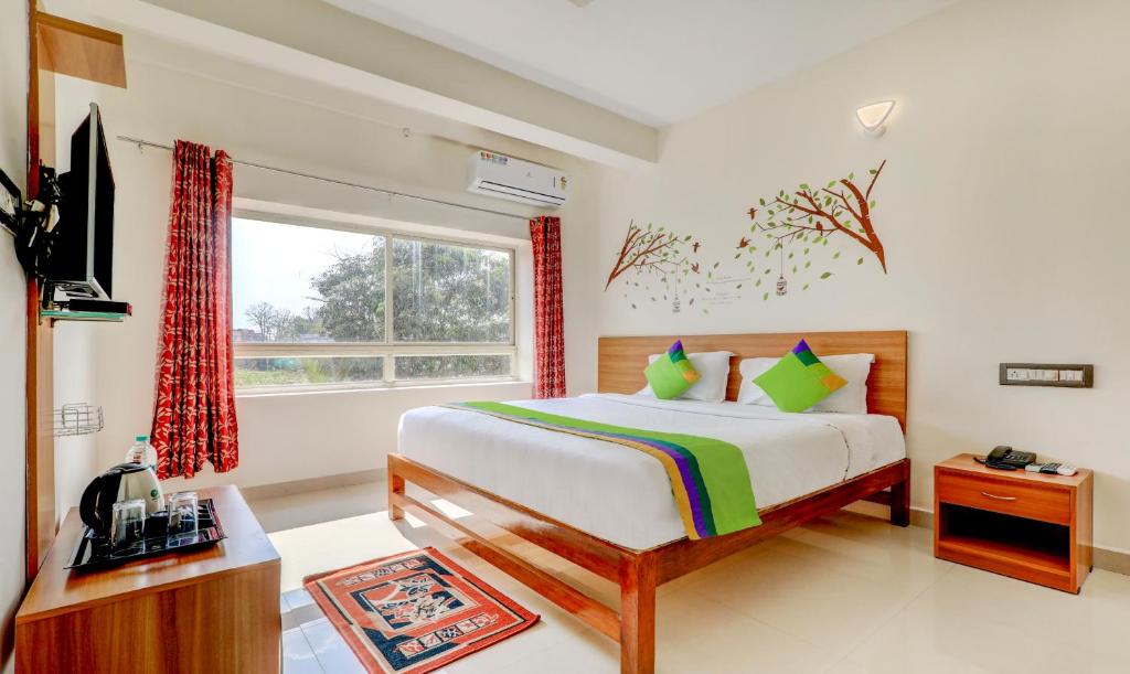 a bedroom with a bed and a tv and a window at Treebo Trend Atithi Comforts 1 Km From Nisargadhama Forest in Kushālnagar