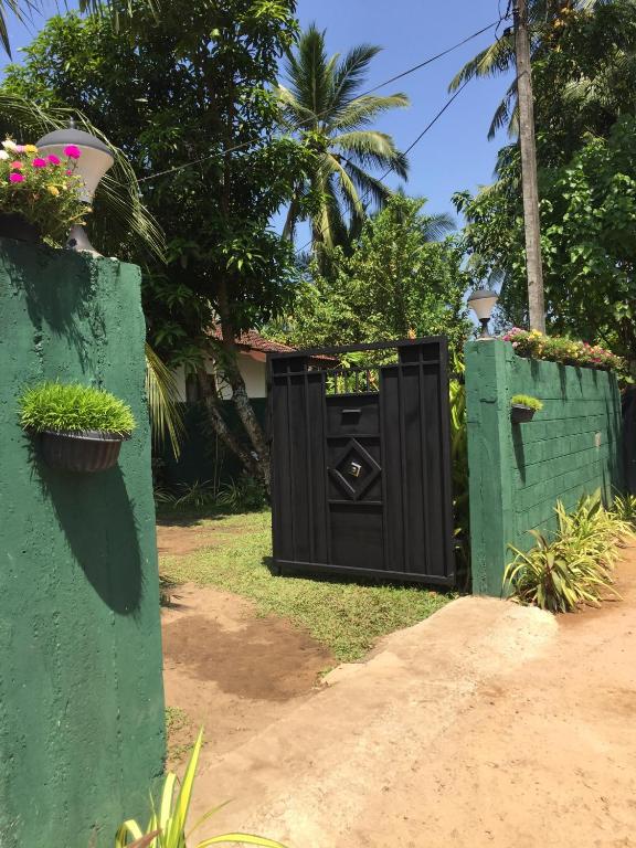 een zwarte poort in een tuin met twee groene hekken bij Grandfather Villa in Kosgoda