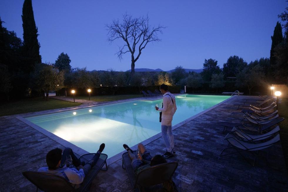 un hombre de pie junto a una piscina por la noche en Hotel & Spa Villa dei Mosaici, en Spello