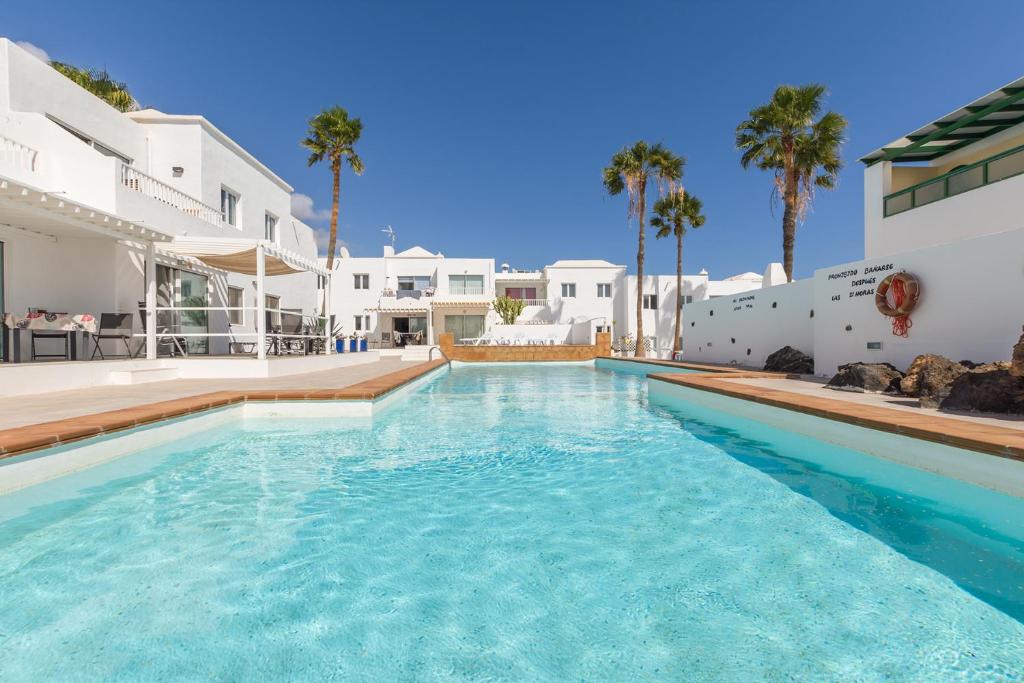 - une piscine en face d'une maison avec des palmiers dans l'établissement Conylanza Tabayba Blue, à Costa Teguise