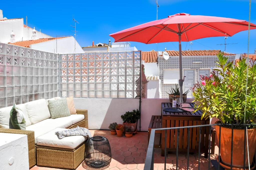 un patio con sofá y sombrilla roja en LovelyStay - Casa Salto - Charming Townhouse with Large Terrace, en Tavira