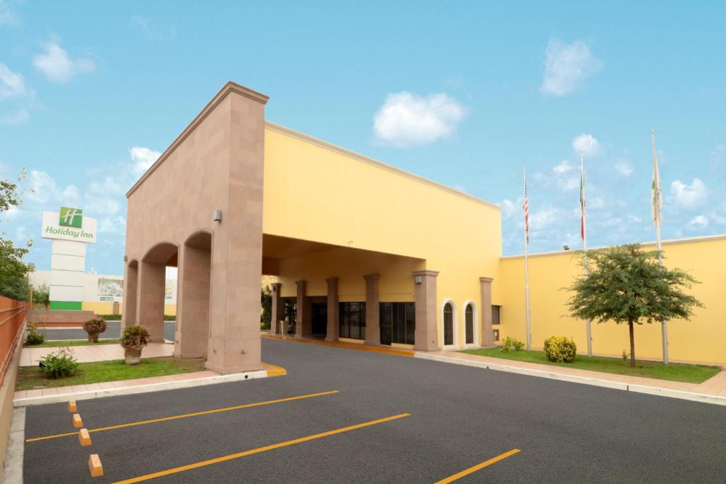 un gran edificio amarillo con banderas en un estacionamiento en Holiday Inn Monterrey Norte, an IHG Hotel en Monterrey