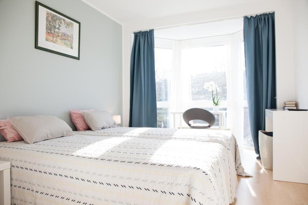 a white bedroom with a large bed with blue curtains at Swetis Passage in Pulheim