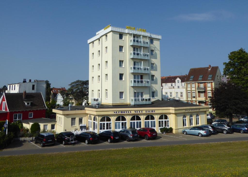 un grand bâtiment blanc avec des voitures garées dans un parking dans l'établissement Seehotel Neue Liebe, à Cuxhaven