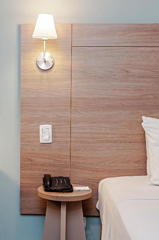 a telephone on a table next to a bed at Slim Curitiba Alto da XV in Curitiba