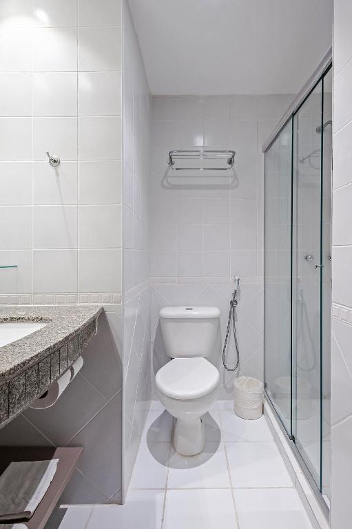 a white bathroom with a toilet and a shower at Slim Curitiba Alto da XV in Curitiba
