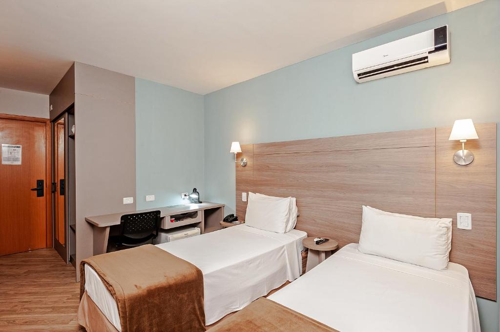 a hotel room with two beds and a desk at Slim Curitiba Alto da XV in Curitiba