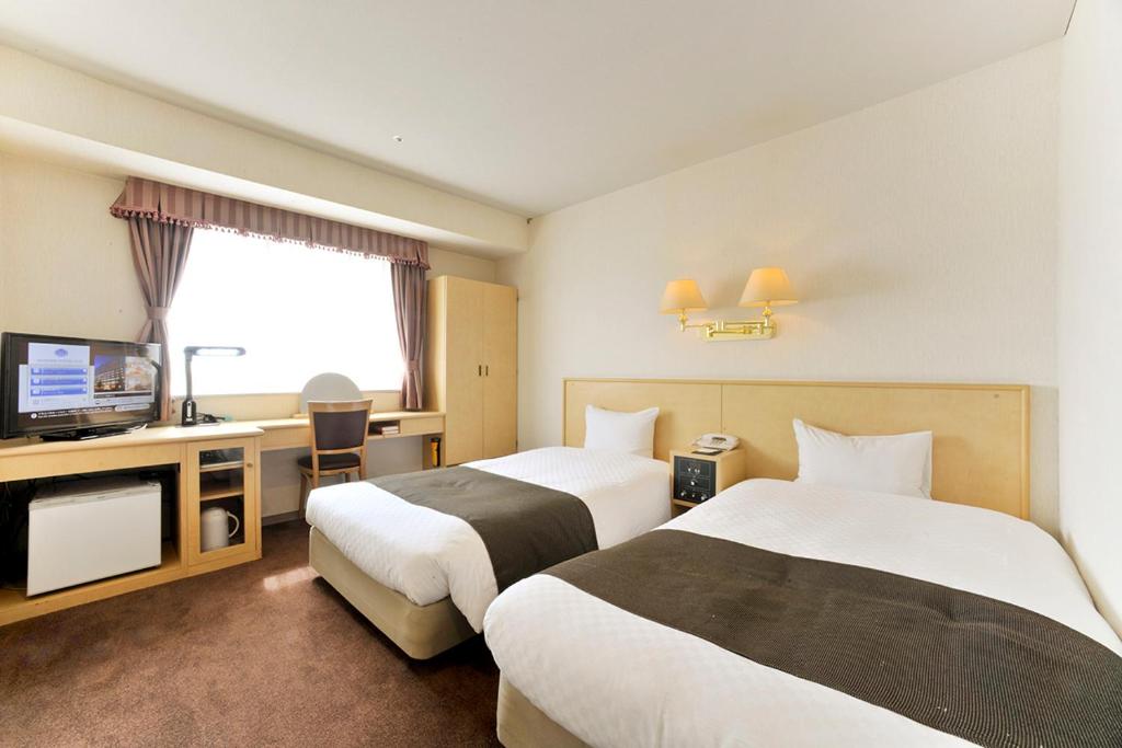 山形市にある山形国際ホテルのベッド2台とテレビが備わるホテルルームです。