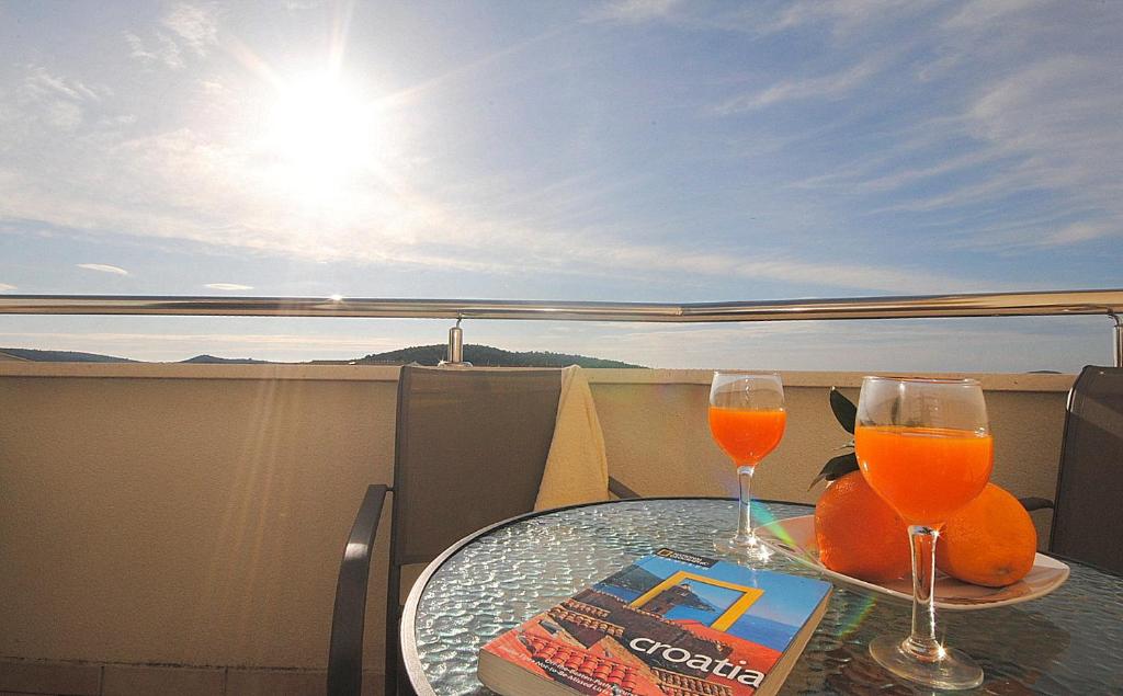 einen Tisch mit zwei Gläsern Orangensaft und ein Buch in der Unterkunft Apartment NOEL in Rogoznica