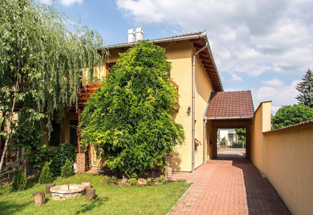 a house with a large green tree next to a walkway at Aqua Apartman in Gyula