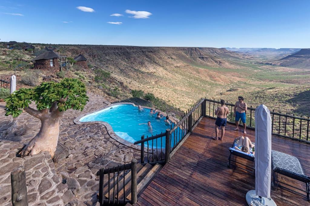eine Gruppe von Personen, die um einen Pool auf einer Terrasse stehen in der Unterkunft Grootberg Lodge in Damaraland