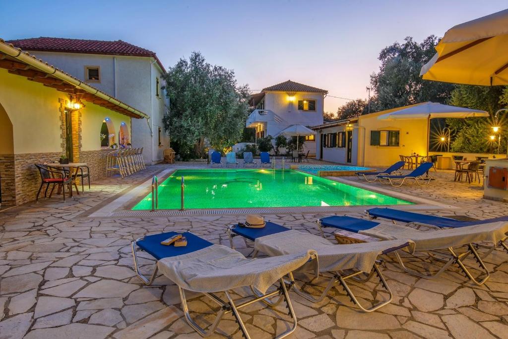 a swimming pool with tables and chairs in front of a house at Olympia Paxos Villas & Apartments in Gaios