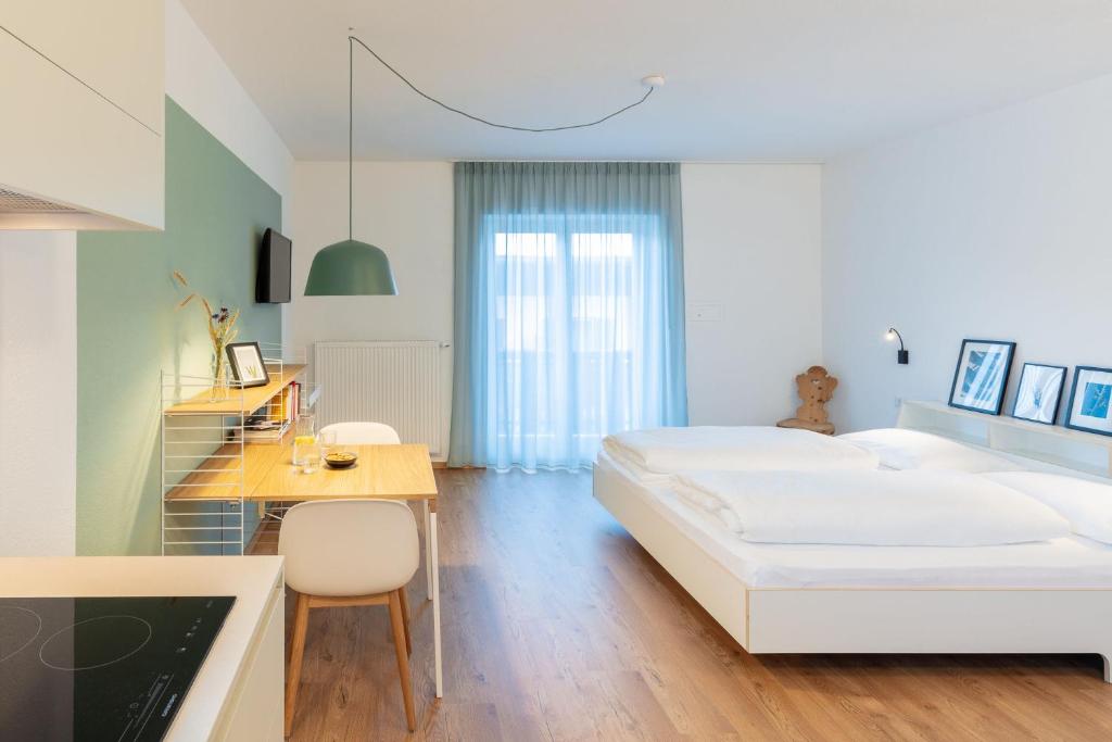 a white bedroom with a bed and a desk and a table at Hus Appartement - Nr. 1 in Valdaora