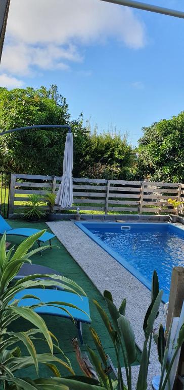 a pool with two chairs and a white umbrella at Meublé chez Gilbert in Le Tampon