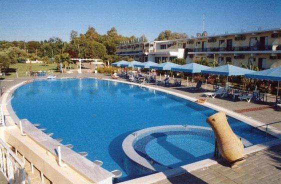 a large swimming pool in a resort with blue umbrellas at Lintzi Hotel in Arkoudi