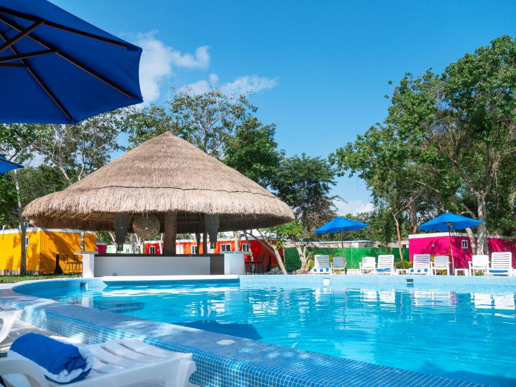 a swimming pool with chairs and a straw umbrella at Colorbox beds and rooms in Tulum