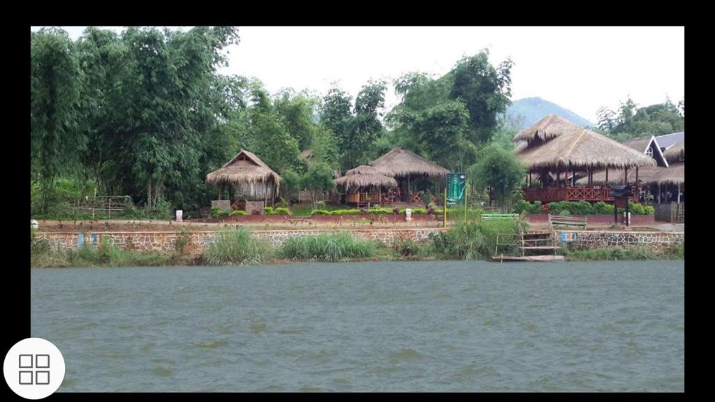 a group of buildings with thatched roofs and a body of water at Bamboo Forest River View Hostel in Ywama