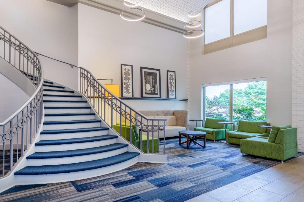 a spiral staircase in a lobby with green chairs at Holiday Inn Express & Suites Chicago-Midway Airport by IHG in Bedford Park