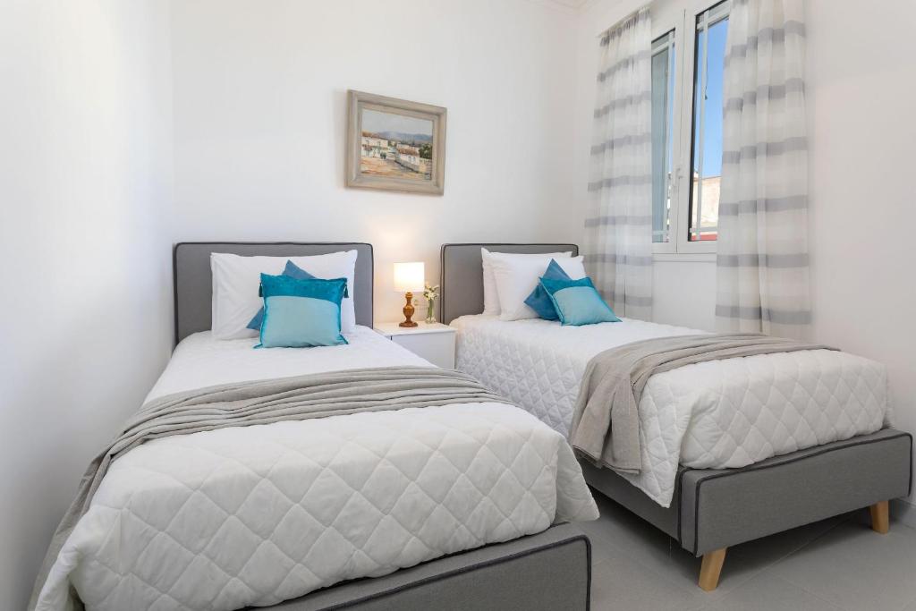 two beds in a white room with blue pillows at Andriani Apartment in Zakynthos Town