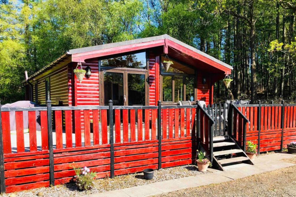 ein rotes winziges Haus mit einem roten Zaun in der Unterkunft Lomond Lodge in Rowardennan