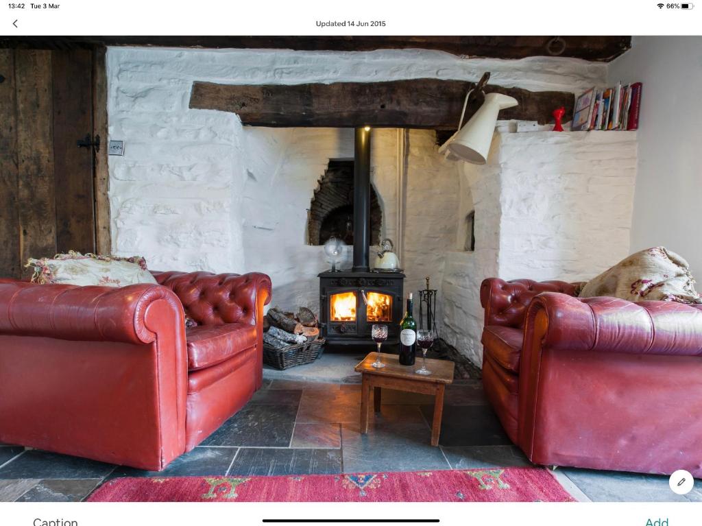 a living room with two red leather couches and a fireplace at Ty Fferm Hen, The Ancient Farmhouse in Talybont